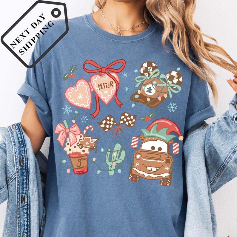 A woman wearing a blue t-shirt with a Christmas-themed design featuring various holiday-related items such as hearts, candy canes, and a character from the Cars movie franchise.