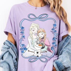 A woman wearing a purple t-shirt with a graphic design featuring two cartoon girls and a snowman.