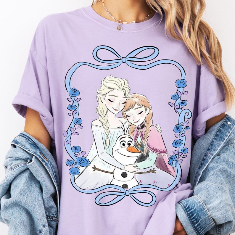 A woman wearing a purple t-shirt with a graphic design featuring two cartoon girls and a snowman.