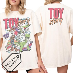 A woman wearing a white t-shirt with a colorful graphic of characters from the Toy Story movie, including Woody and Buzz Lightyear.