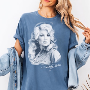A woman wearing a blue t-shirt with a portrait of a woman printed on it, along with a denim jacket.