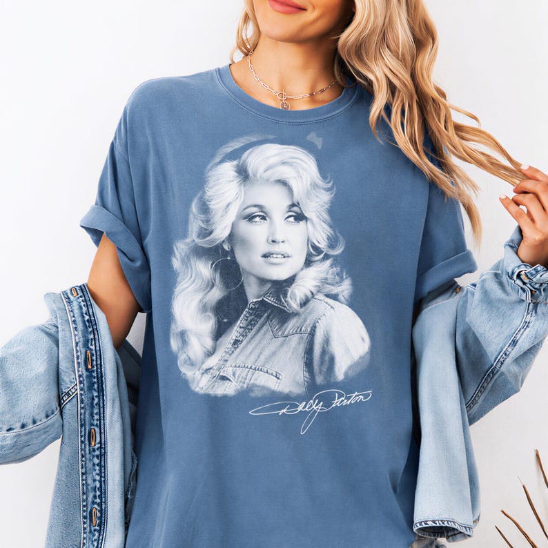 A woman wearing a blue t-shirt with a portrait of a woman printed on it, along with a denim jacket.