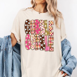 A woman wearing a white t-shirt with the word "GOBBLE GOBBLE" printed on it, along with various colorful and patterned designs.