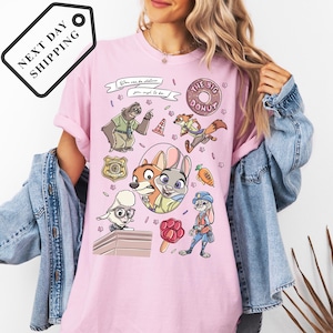 A woman wearing a pink t-shirt with a cartoon character design featuring various animals and objects, such as a police officer, a police dog, and a donut.