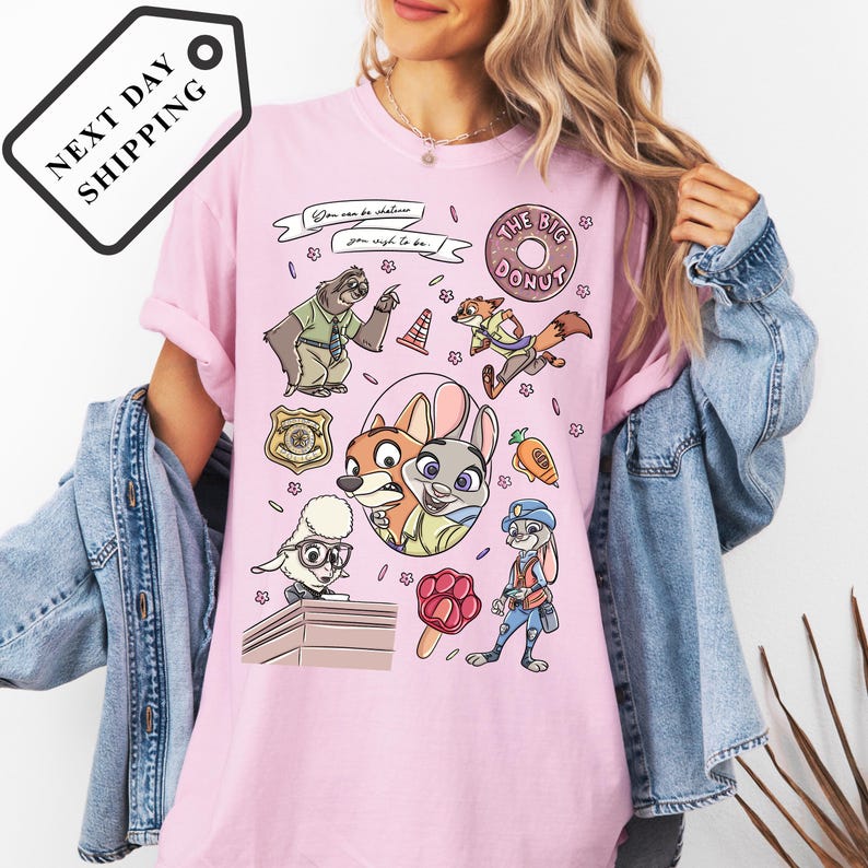 A woman wearing a pink t-shirt with a cartoon character design featuring various animals and objects, such as a police officer, a police dog, and a donut.