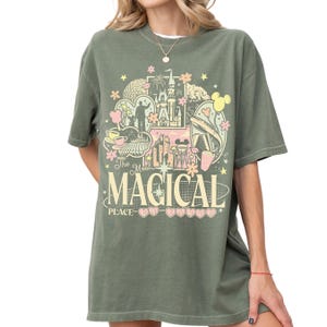 A woman wearing a green t-shirt with a graphic design featuring various Disney-themed elements such as Mickey Mouse, castles, and other iconic imagery.