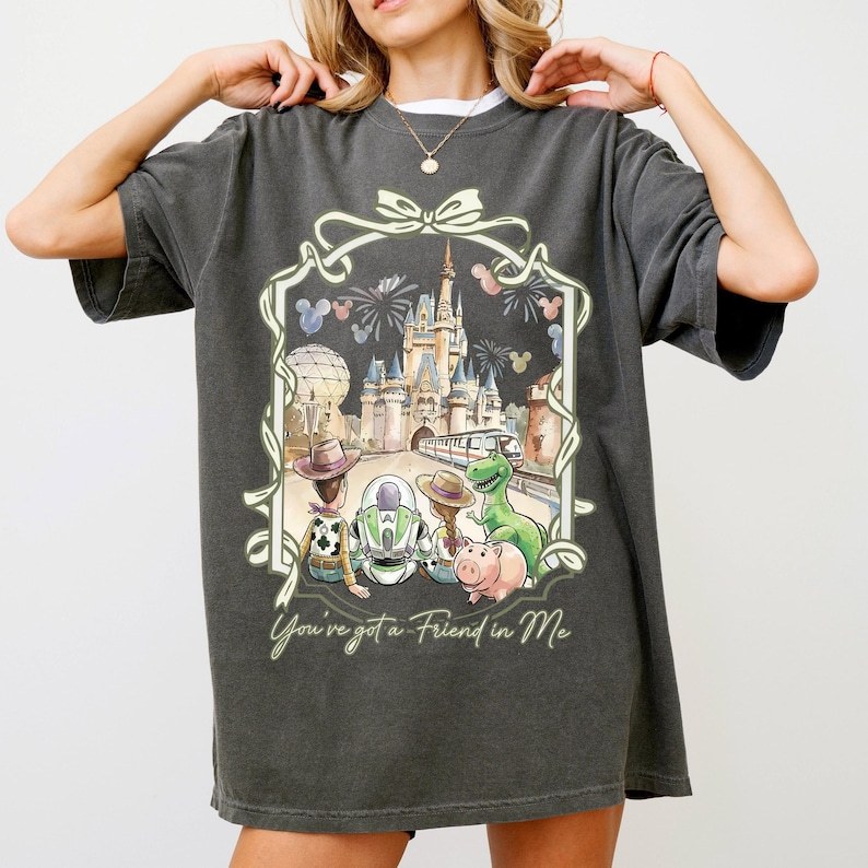 A woman wearing a gray t-shirt with a graphic design featuring a castle, a dinosaur, and various other characters.