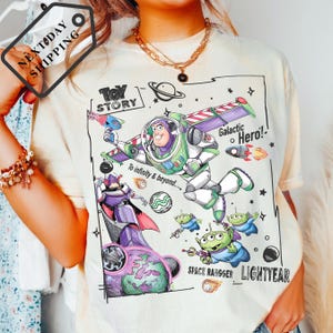 A person wearing a white t-shirt with a colorful graphic design featuring characters from the Toy Story franchise, including Buzz Lightyear and a space ranger.