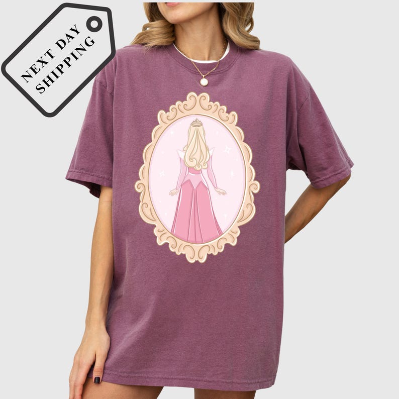 A woman wearing a purple t-shirt with a graphic of a woman in a pink dress.