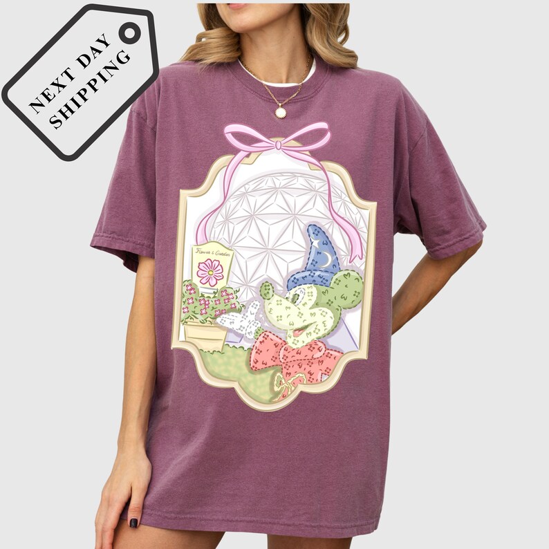 A woman wearing a purple t-shirt with a graphic design featuring a cartoon character and various decorative elements.
