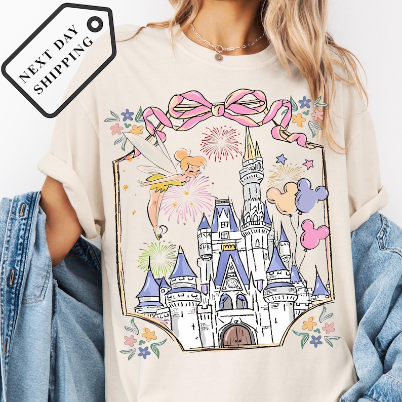 A person wearing a white t-shirt with a colorful illustration of a castle and fireworks on it.
