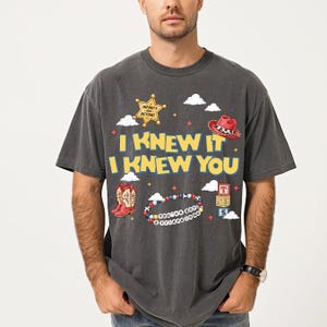 A man wearing a gray t-shirt with a graphic design featuring various cartoon-style icons and text.