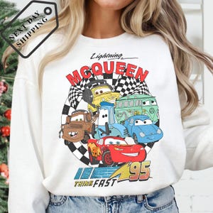 A person wearing a white long-sleeved shirt with a graphic design featuring characters from the animated movie "Cars".