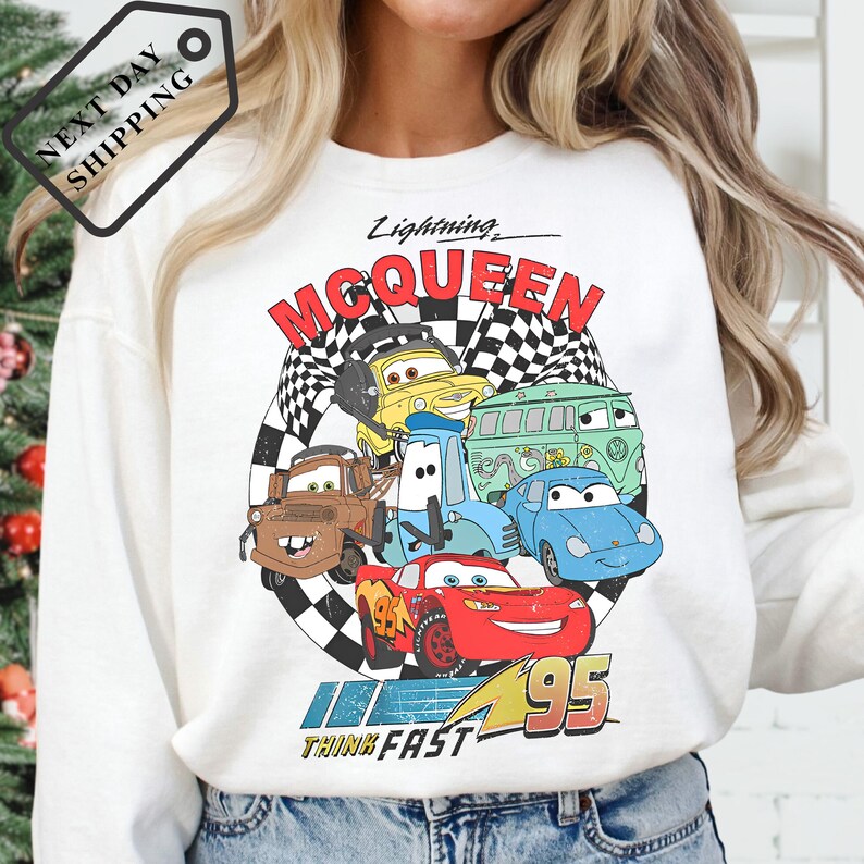 A person wearing a white long-sleeved shirt with a graphic design featuring characters from the animated movie "Cars".