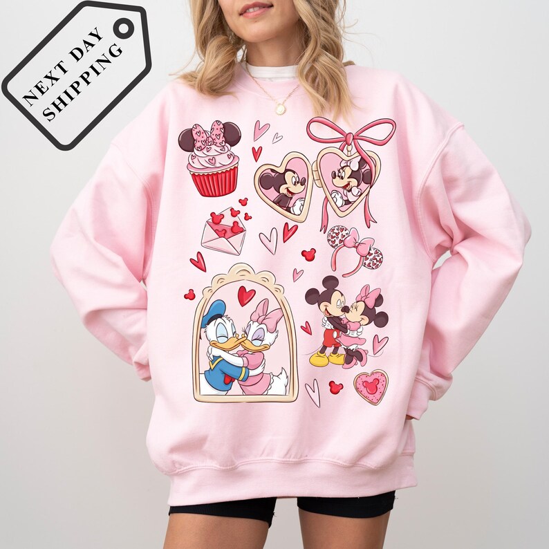 A woman wearing a pink sweatshirt with a Disney-themed design featuring Minnie Mouse, Donald Duck, and other Disney characters.