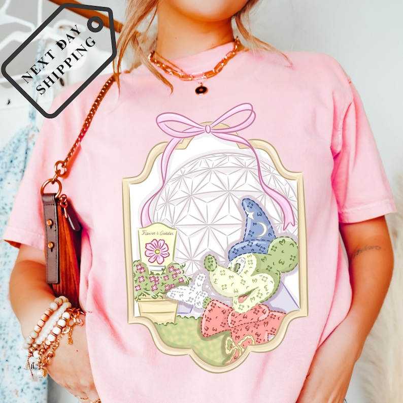 A woman wearing a pink t-shirt with a graphic of Mickey Mouse and a flower, along with a necklace and a brown purse.