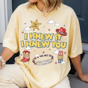 A person wearing a yellow t-shirt with a cartoon-style design and text printed on it.