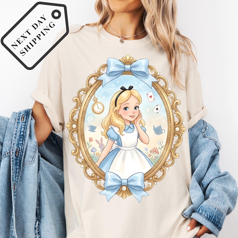 A woman wearing a white t-shirt with a graphic of a young girl in a blue dress and a clock, surrounded by a decorative frame.