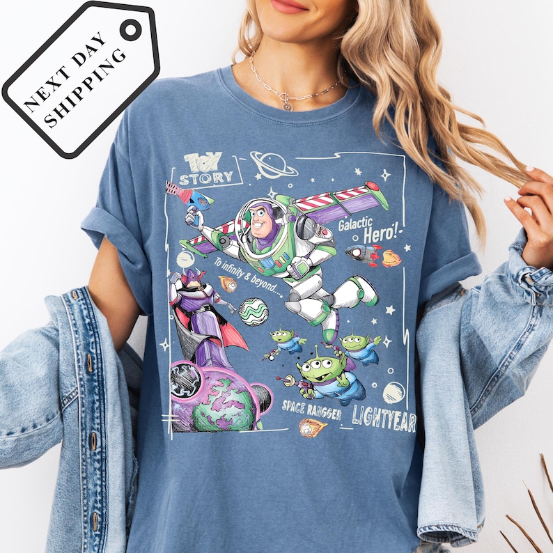 A woman wearing a blue t-shirt with a graphic design featuring characters from the Toy Story franchise, including Buzz Lightyear and a space ranger, along with various space-themed elements.