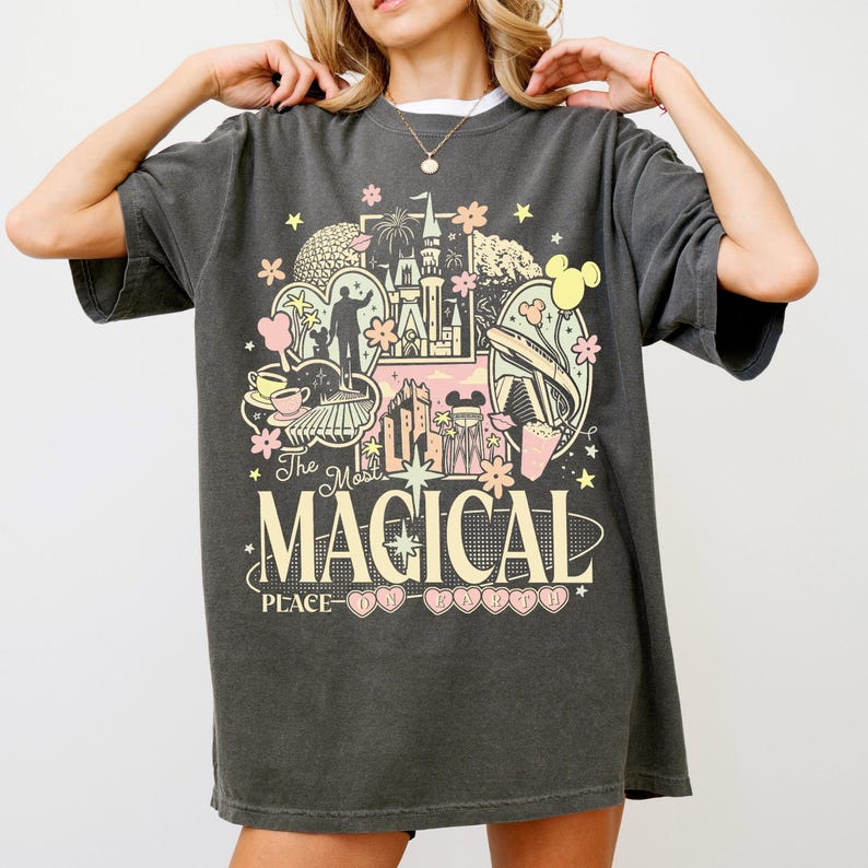 A woman wearing a gray t-shirt with a colorful graphic design featuring various Disney-themed elements such as Mickey Mouse, the Eiffel Tower, and other iconic landmarks.