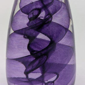 May include: A clear glass paperweight with a swirling purple design inside. The design is reminiscent of smoke or a cloud.