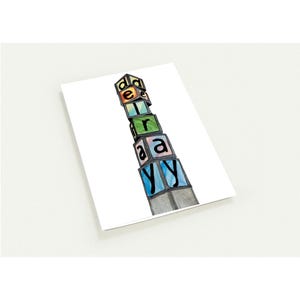 May include: A watercolor illustration of a stack of colorful alphabet blocks spelling out the word "d-e-l-r-a-y". The blocks are in shades of blue, green, yellow, and pink, with black letters. The artwork is on a white background.
