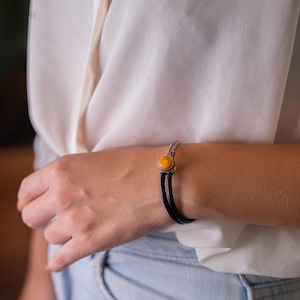 May include: A black leather bracelet with a silver chain and a yellow amber stone.