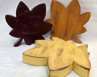 May include: Three wooden leaf decorations in shades of burgundy, golden yellow, and light brown. Each leaf has a rustic, distressed finish and a three-dimensional design, perfect for fall decor.