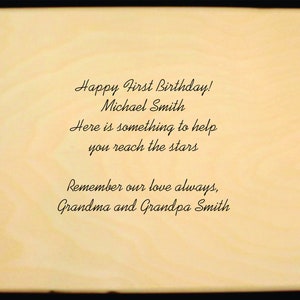 Puede incluir: Placa de madera de color claro con texto negro. El texto dice: "&iexcl;Feliz primer cumplea&ntilde;os! Michael Smith. Aqu&iacute; hay algo para ayudarte a alcanzar las estrellas. Recuerda siempre nuestro amor, abuela y abuelo Smith."