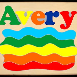 May include: A wooden puzzle with the name "Avery" spelled out in colorful letters. The puzzle has a rainbow design with wavy lines in red, orange, yellow, green, blue, and light blue.