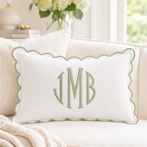 May include: A rectangular white throw pillow featuring a scalloped edge trimmed in sage green. The center of the pillow displays a large, embroidered monogram in sage green thread with the letters J, M, and B in a classic serif font style.