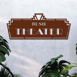 May include: A brown metal sign with a decorative art deco design. The sign reads "Bush Theater" in white lettering.