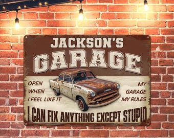 Puede incluir: Un letrero de metal marrón oxidado con el texto "JACKSON'S GARAGE" en blanco. El letrero también incluye el texto "OPEN WHEN I FEEL LIKE IT" y "MY GARAGE MY RULES" en blanco. El letrero presenta un automóvil antiguo marrón oxidado con un cuerpo blanco y un fondo blanco.