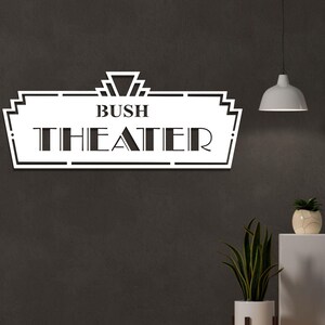 May include: White metal sign with a black art deco design. The sign reads "Bush Theater".
