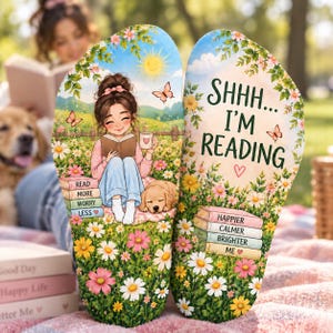 May include: A pair of flip-flops featuring a printed illustration of a person reading a book in a field of flowers with a dog. The left sandal shows the person and dog, while the right sandal displays the text SHHH... I'M READING and stacked books.