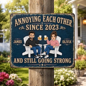 Può includere: Una targa rettangolare in metallo con sfondo blu scuro testurizzato e il testo ANNOYING EACH OTHER SINCE 2023 AND STILL GOING STRONG. Raffigura due personaggi disegnati seduti su sedie bianche, con boccali di birra, etichettati JAMES e OLIVIA.