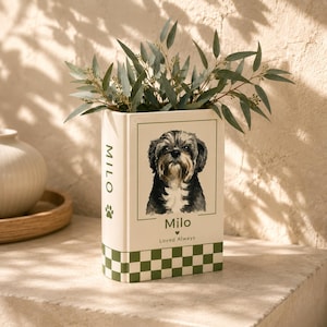 May include: A rectangular off-white ceramic vase shaped like a book, featuring a watercolor illustration of a dog, the name Milo, and the text Loved Always. The base has a green and white checkered pattern, and the side displays the name Milo.
