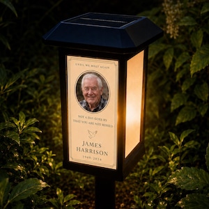 May include: A black solar-powered memorial lantern with a rectangular frame and a top solar panel. The front panel features a portrait of an older man, the text UNTIL WE MEET AGAIN, NOT A DAY GOES BY THAT YOU ARE NOT MISSED, JAMES HARRISON, 1948-2024.