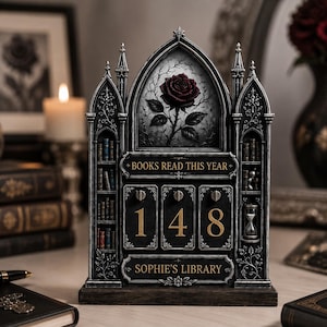 May include: A dark gray gothic-style book tracker display featuring a central arch with a red rose illustration. It includes the text "BOOKS READ THIS YEAR" and "SOPHIE'S LIBRARY" with three rotating number dials currently set to 148 and miniature shelves.