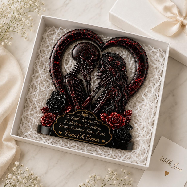 May include: A heart-shaped decorative sculpture featuring two skeletons facing each other, finished in black and red with a cracked texture. The base includes red and black roses and a plaque with the text: In Death, We Are One. In Darkness, We Belong. Forever Entwined, Never Apart. Daniel & Emma.