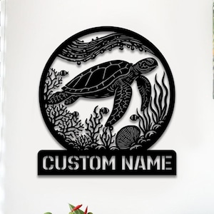 Op de afbeelding: Zwarte metalen wandkunst met een zeeschildpad die in een cirkel zwemt met koraal, zeewier en bubbels. De tekst "CUSTOM NAME" staat onder de cirkel.