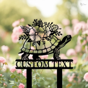 Op de afbeelding: Zwarte metalen tuinpaal met een schildpad die een boeket bloemen draagt. De paal heeft een bord met de tekst "CUSTOM TEXT".