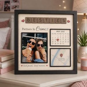 May include: A square black-framed wall art piece featuring the word BESTIES in wooden tiles, the text Partners In Crime, and Good friends. Great memories. It includes a photo of two people eating ice cream, a May 2012 calendar, and a Central Park map.