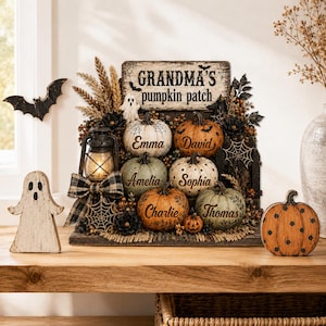 Puede incluir: Una decoración de Halloween con un letrero que dice Grandma's pumpkin patch, seis calabazas personalizadas con los nombres Emma, David, Amelia, Sophia, Charlie y Thomas, una linterna, un fantasma y detalles de murciélagos negros.