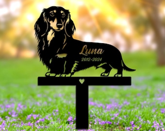 May include: Black metal silhouette of a dachshund dog with the name "Luna" and the dates "2019-2024" engraved on the base. The silhouette is mounted on a black metal stake with a heart cutout.