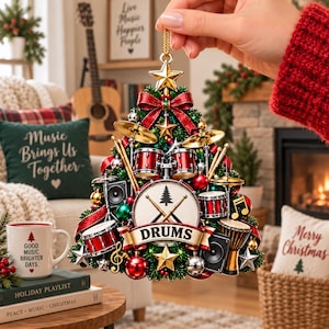 May include: A Christmas tree-shaped ornament featuring a drum kit design with red drums, gold cymbals, and black speakers. The center displays a white drum head with a tree icon and crossed drumsticks, with a banner reading DRUMS at the base.