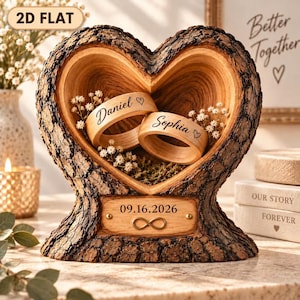 May include: A heart-shaped wooden ring holder with rough bark edges, featuring two light wood rings engraved with the names Daniel and Sophia. A central plaque displays the date 09.16.2026 and an infinity symbol. Small white flowers decorate the interior.