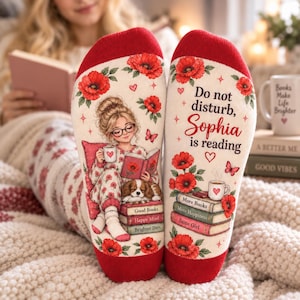 May include: A pair of white socks with red trim featuring a graphic of a person with glasses reading a book with a dog, red poppies, and butterflies. The text reads: Do not disturb, Sophia is reading, More Books, More Happiness, Same Girl.