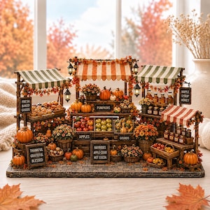 May include: A miniature autumn market display featuring wooden stalls with striped awnings, decorated with orange and yellow fall foliage. The stalls display pumpkins, gourds, apples, baked goods, and jars labeled Maple Syrup and Honey.