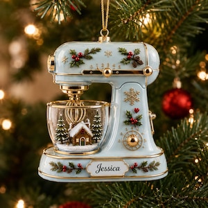 Könnte beinhalten: Ein hellblauer Weihnachtsbaumschmuck in Form einer Küchenmaschine mit goldenen Akzenten, Stechpalmen- und Schneeflockenmotiven sowie einer Glasschüssel mit einer Miniatur-Winterlandschaft aus Haus und Tannen. Der Name Jessica steht auf dem Sockel.